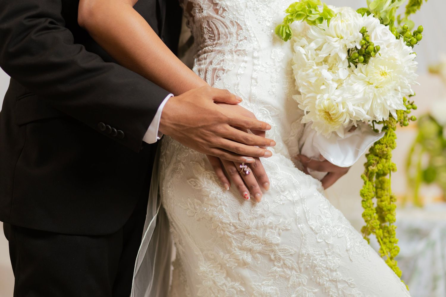 Close-up of bride and groom embracing, bride holding white floral bouquet in lace wedding gown.