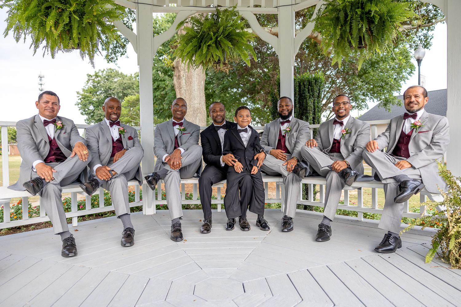 Wedding party dances and poses playfully in front of a white gazebo.