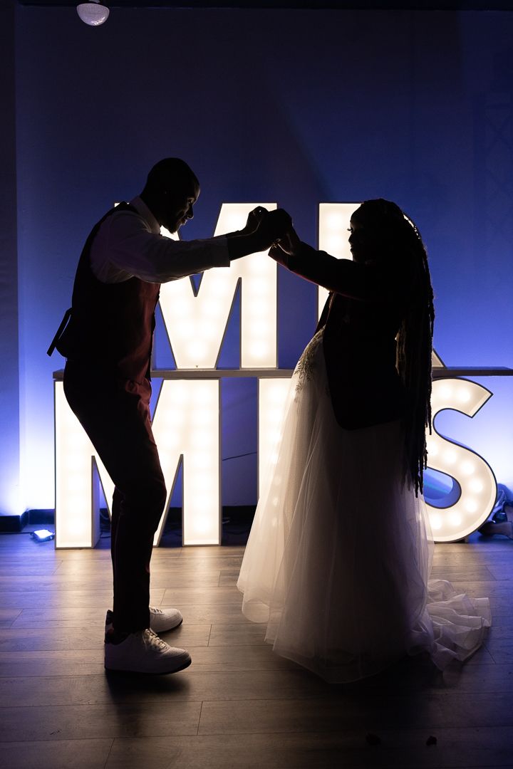 Silhouetted couple poses against backlit letters during wedding photoshoot.