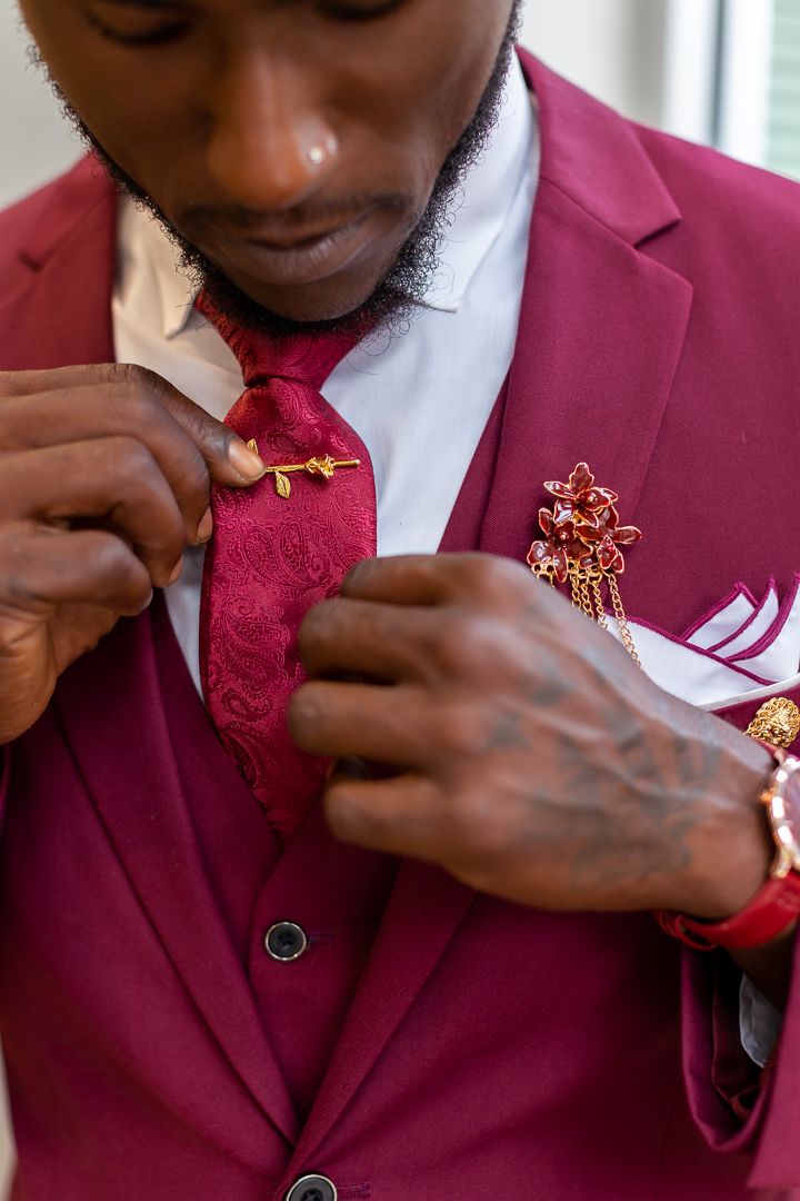 Detail shot of burgundy suit jacket with decorative pin or brooch being adjusted.