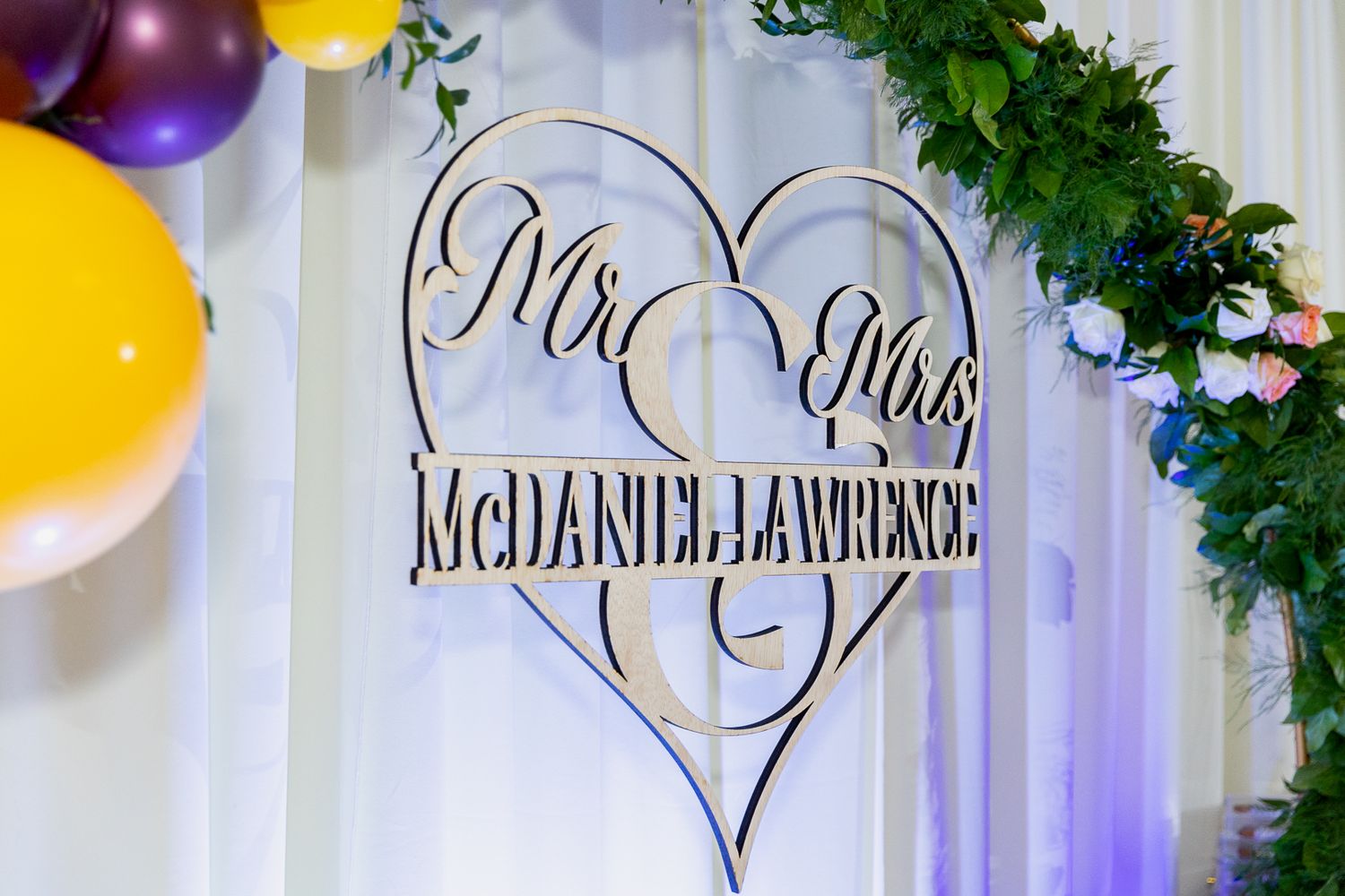 Wedding decor with heart-shaped backdrops, purple and yellow balloons, and greenery garlands creating a romantic atmosphere.