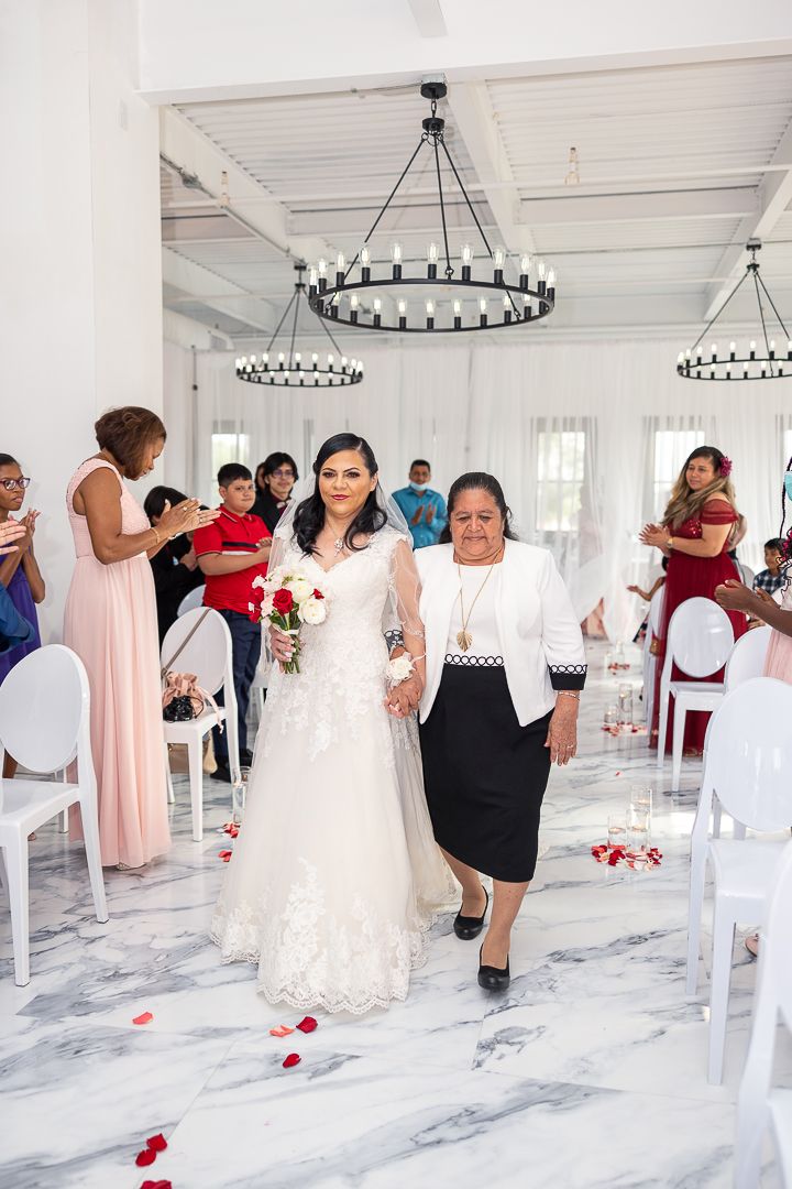 Wedding guests mingle in a bright white reception hall with modern chandeliers and marble floors.