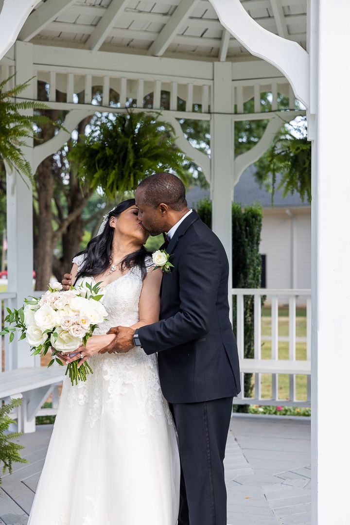 Romantic wedding couple shares intimate moments under white gazebo with hanging plants.