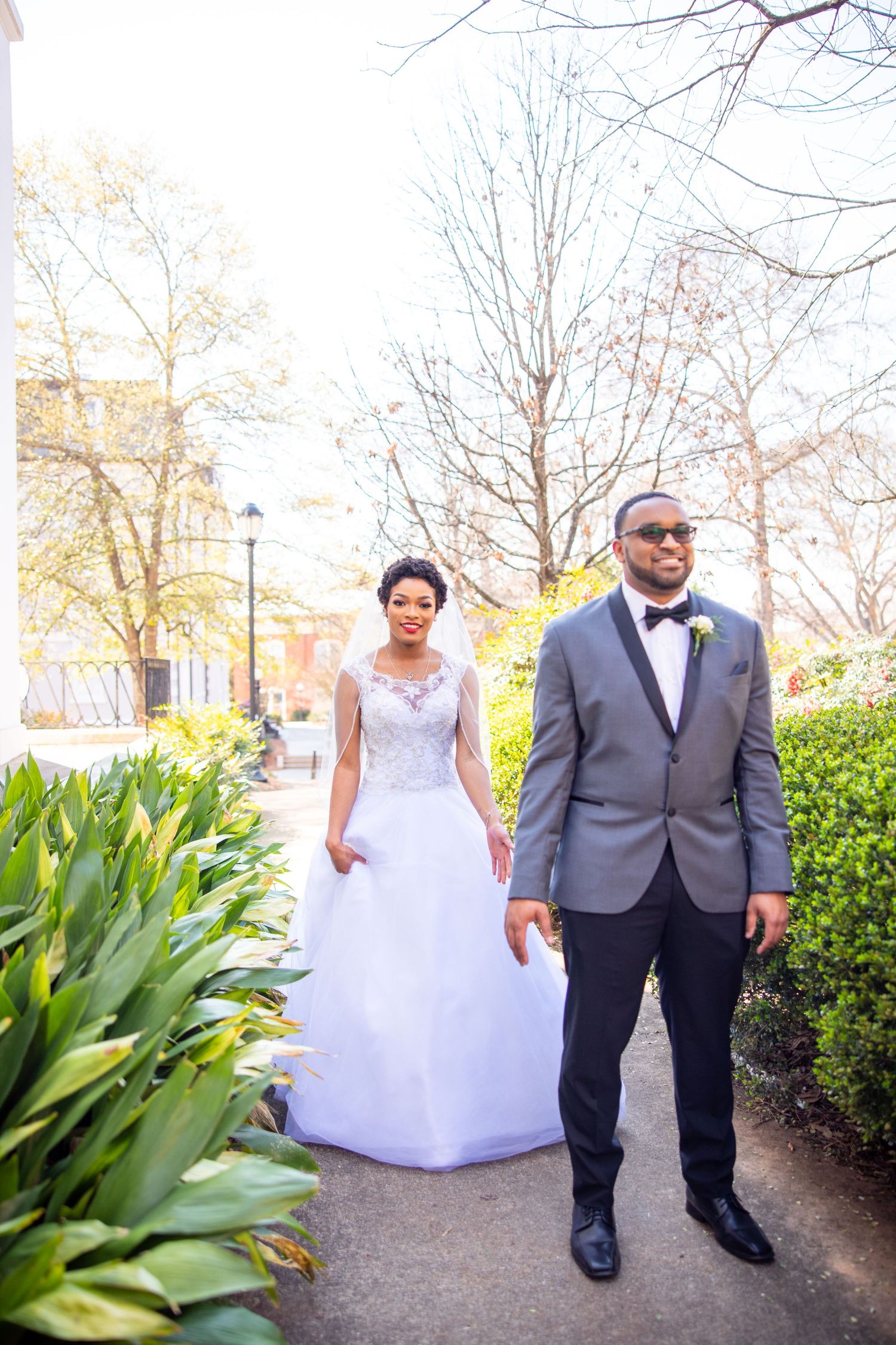 A couple shares a romantic moment while walking along a garden path in their wedding attire.