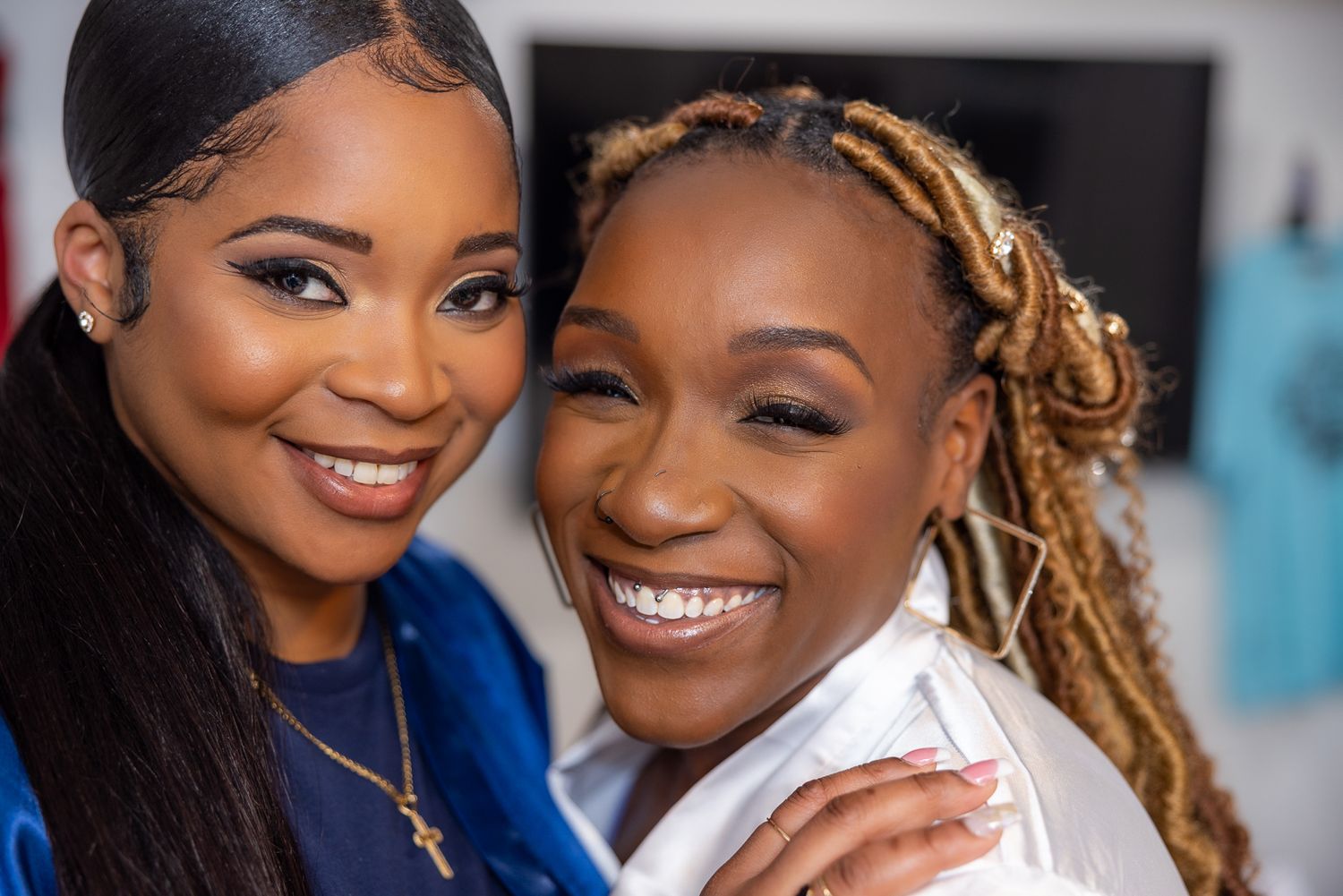Two people sharing a joyful moment with bright smiles and elegant makeup.