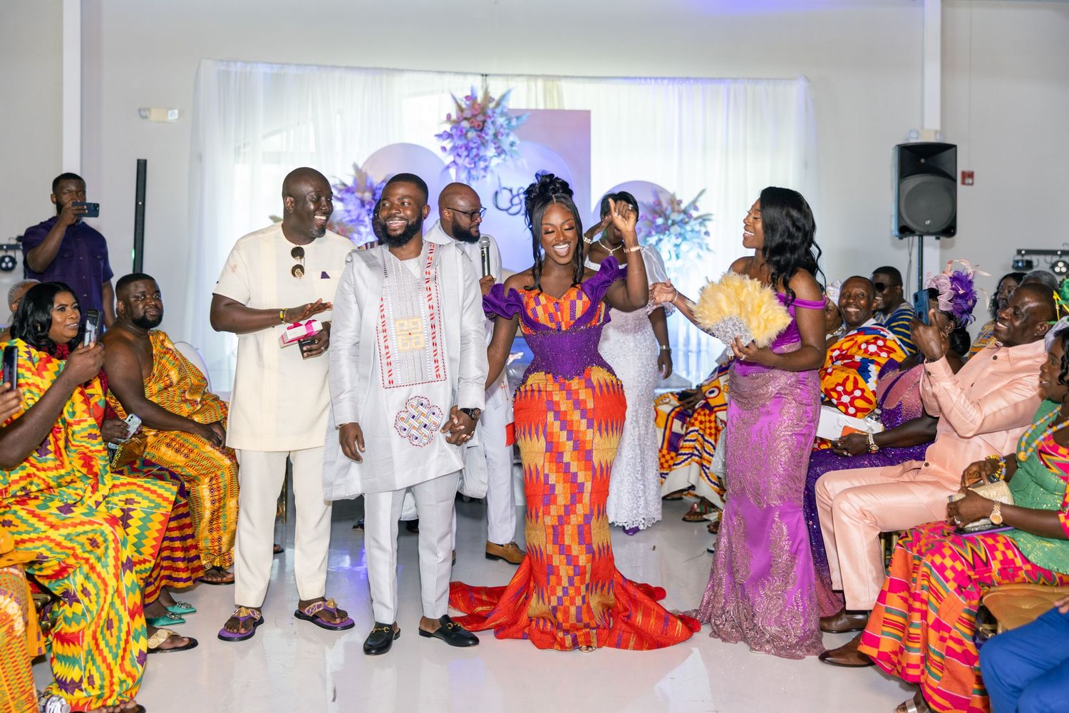 Wide shot of an indoor celebration showing guests in traditional African clothing and formal wear.