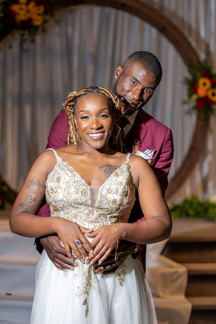 Romantic wedding portraits under wooden arch with white draping and floral accents.