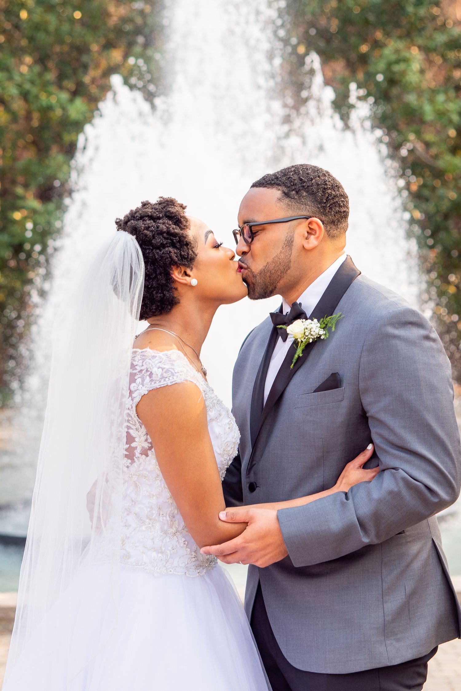 Newlyweds share their first kiss as a married couple in front of a garden fountain.