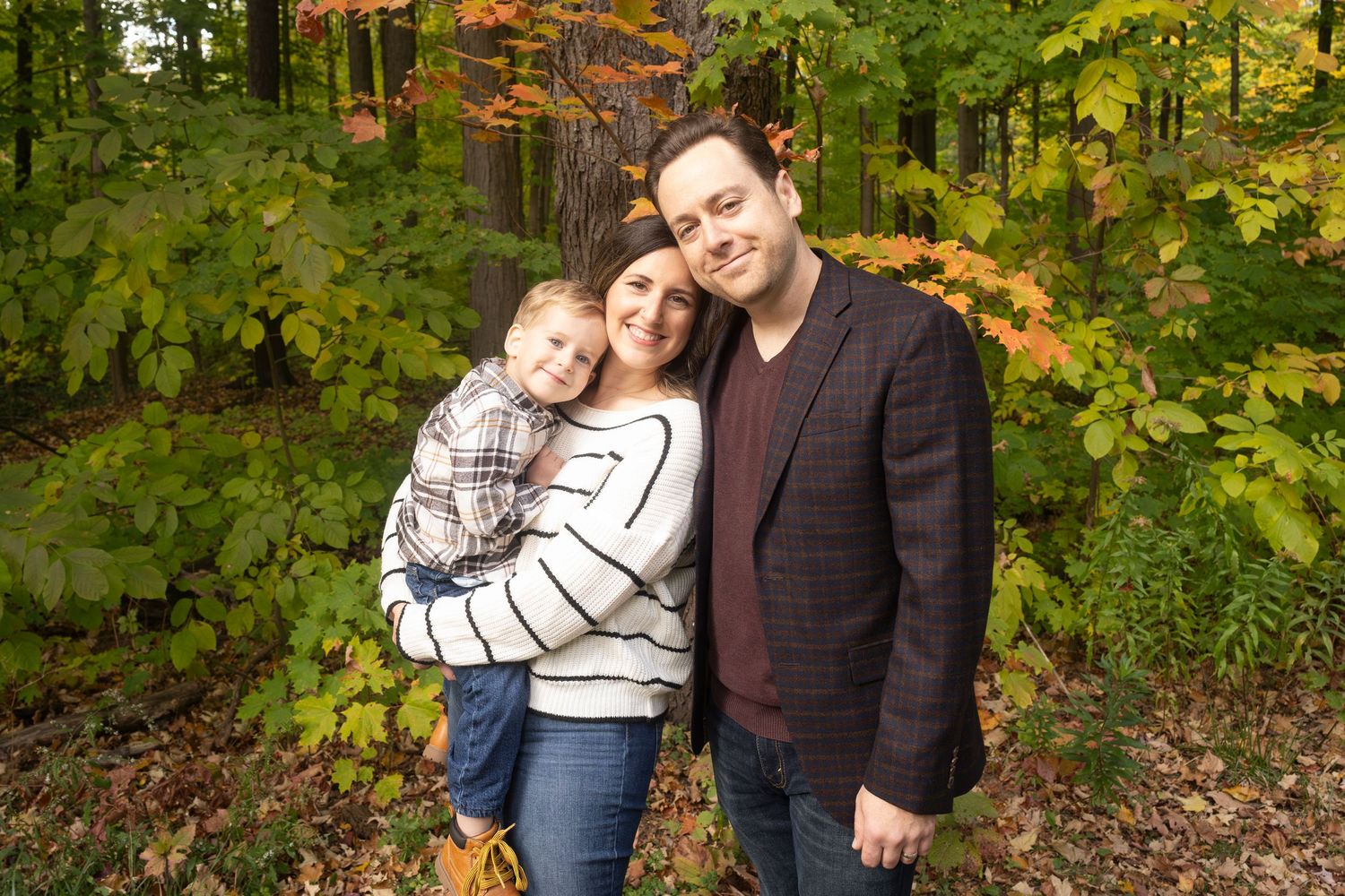 A couple poses together in an autumn forest setting with vibrant fall foliage in the background.