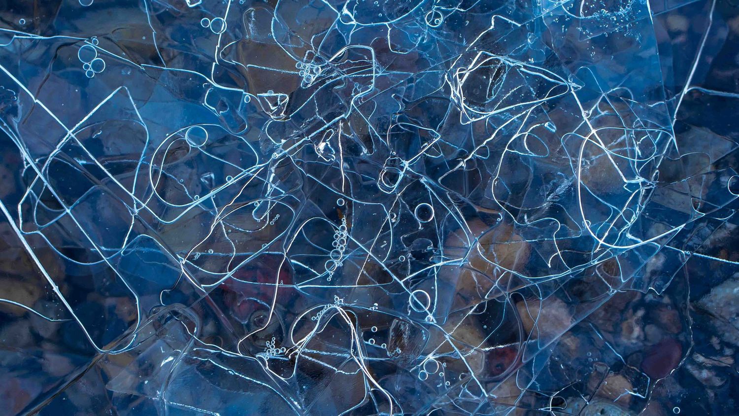 Abstract patterns are created by this thin ice and water over pebbles.