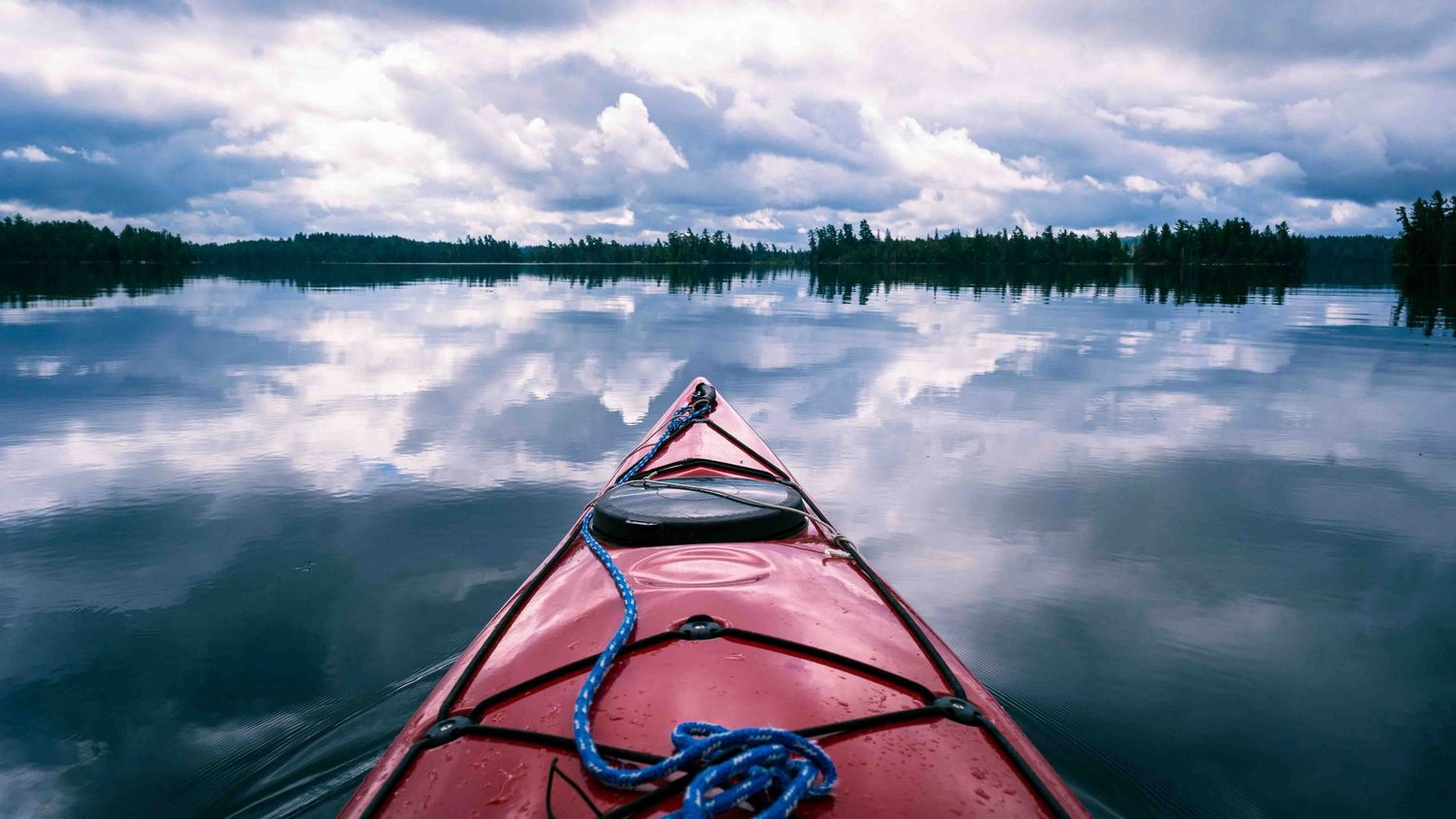 Panoramic landscape view of a kayak and cloudy skies over Lake Temagami lake with evergreen forest in the distance.