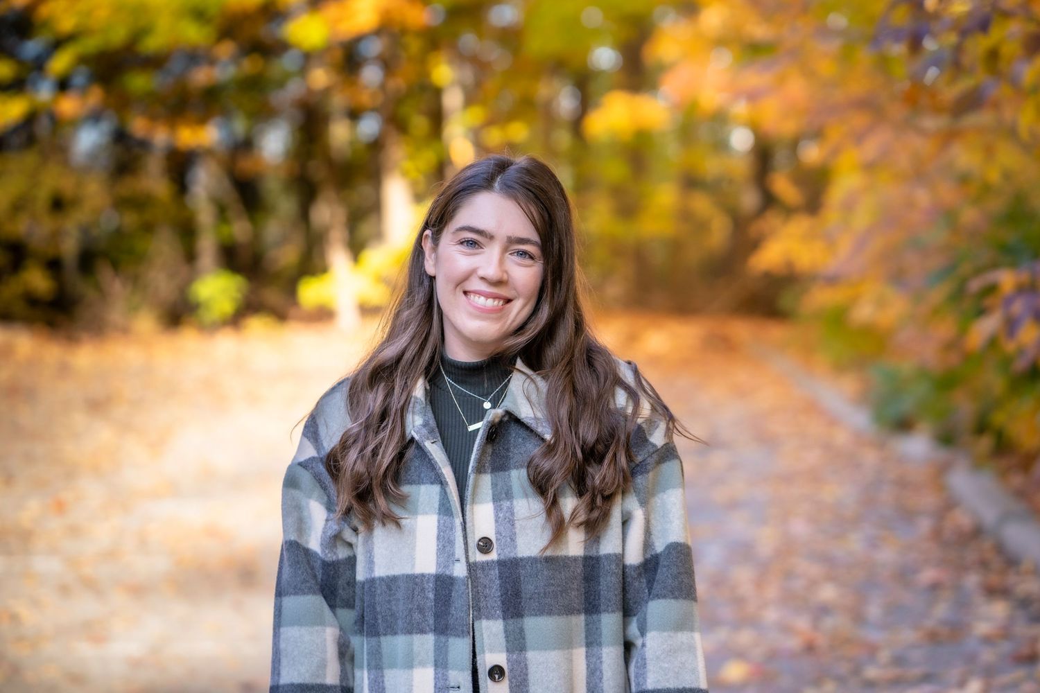 Fall portrait series wearing plaid jacket with autumn foliage in background.