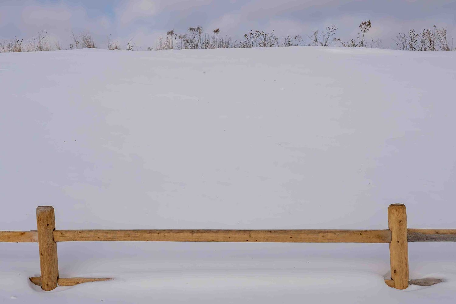 A wooden fence stretches across a snow-covered winter landscape under a blue key for a minimalistic, clean photo