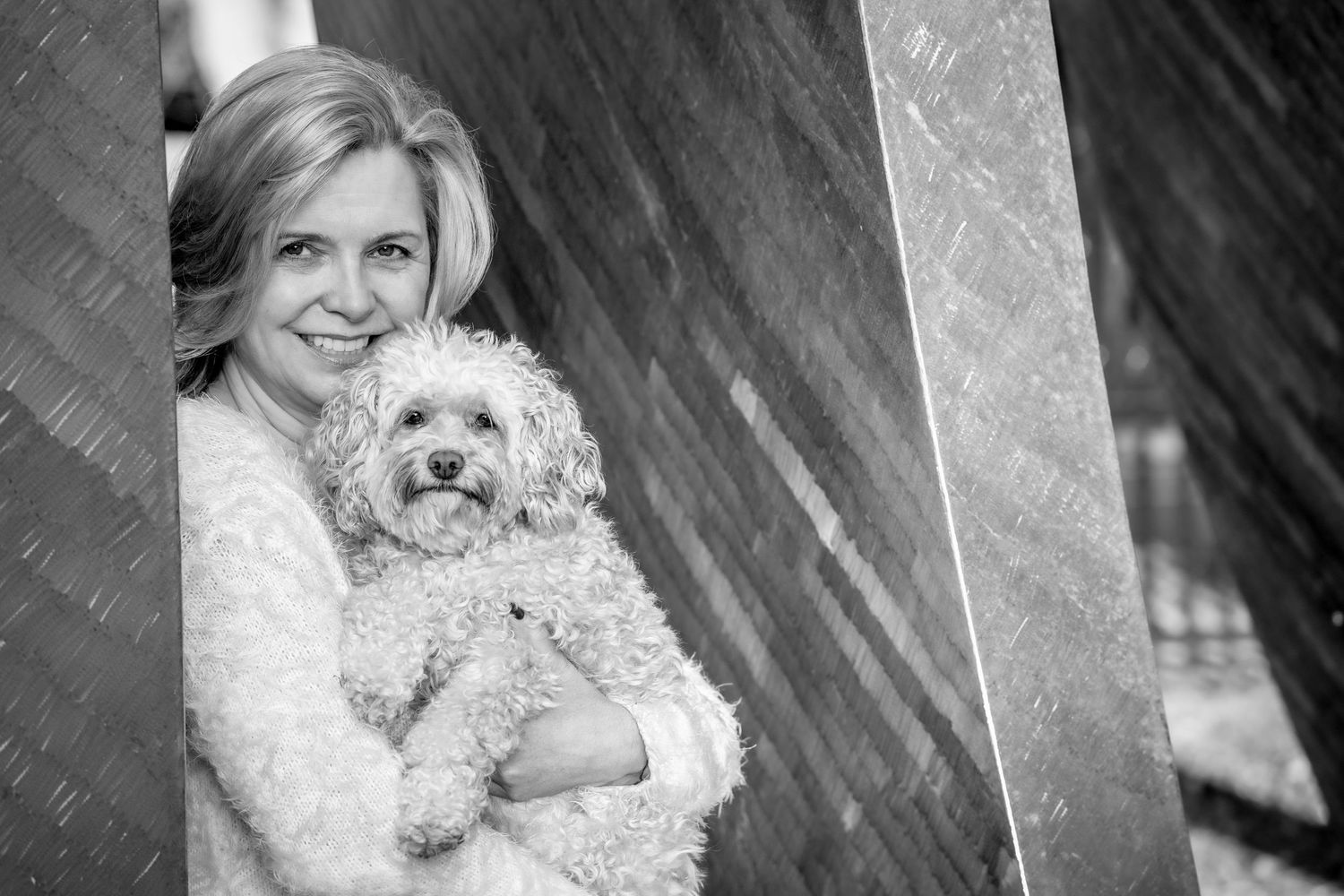 A small white dog is held lovingly in a woman's arms in a black and white portrait.