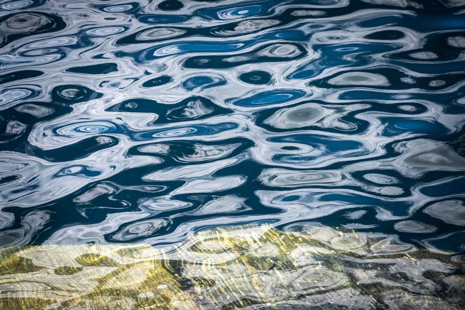 Abstract pattern of rippling blue water and the Canadian shield creates swirling designs and textures.