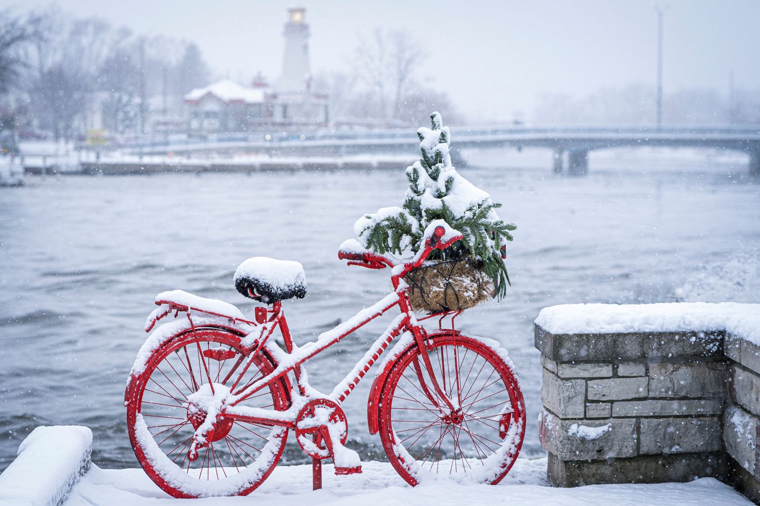Port Credit's red bicycle decorated for Christmas covered in snow against winter backdrop.