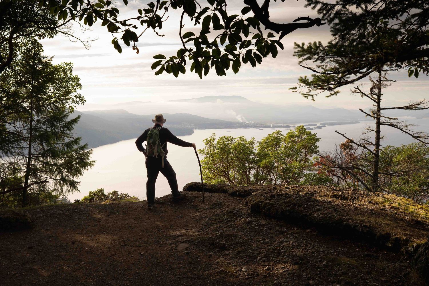 Silhouette of a hiker standing on a cliff edge overlooking a scenic mountain landscape on Saltspring Island.