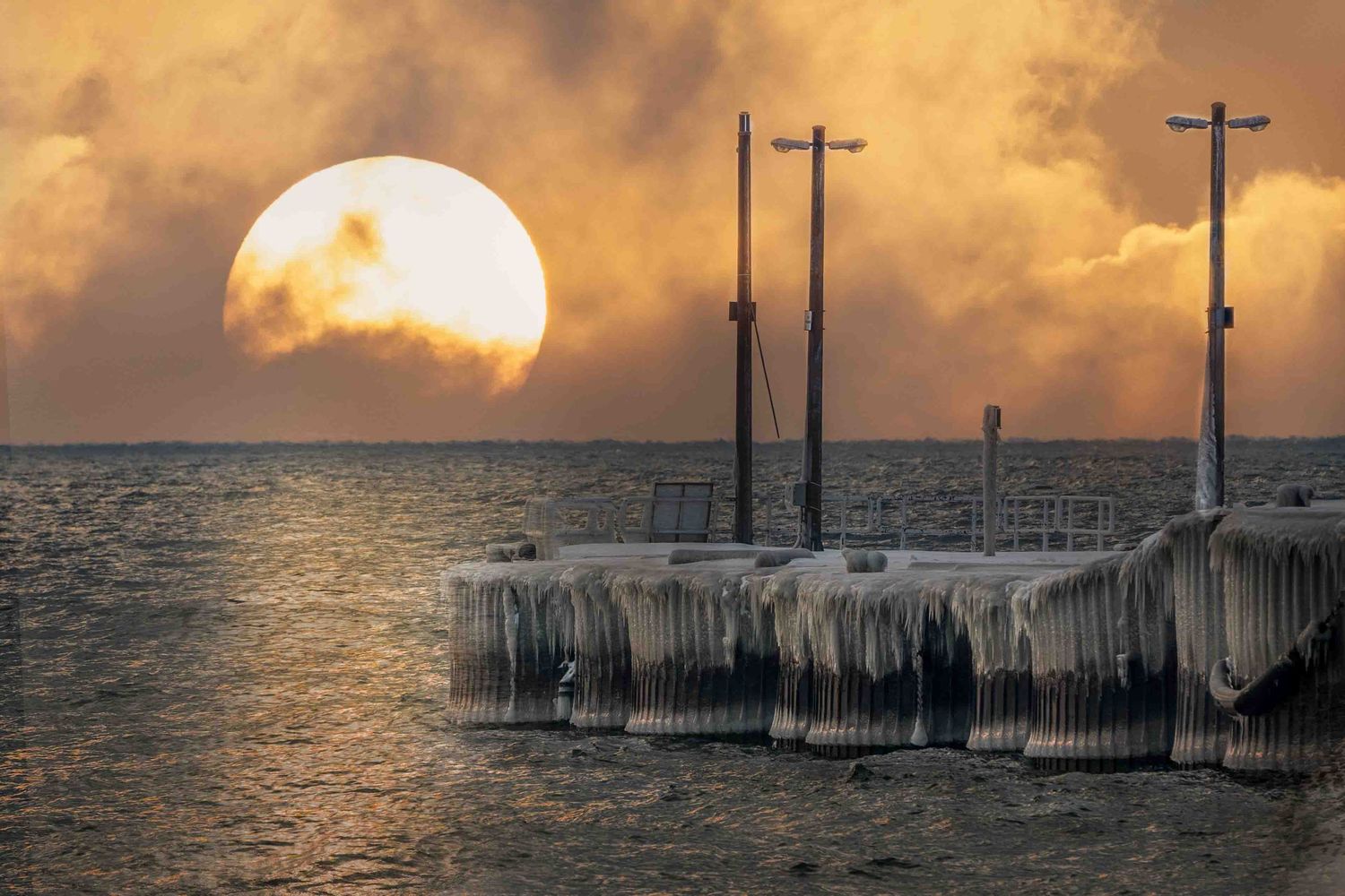 Dramatic orange sunrise over a wintery Lake Ontario with ice-covered pier extended into the water
