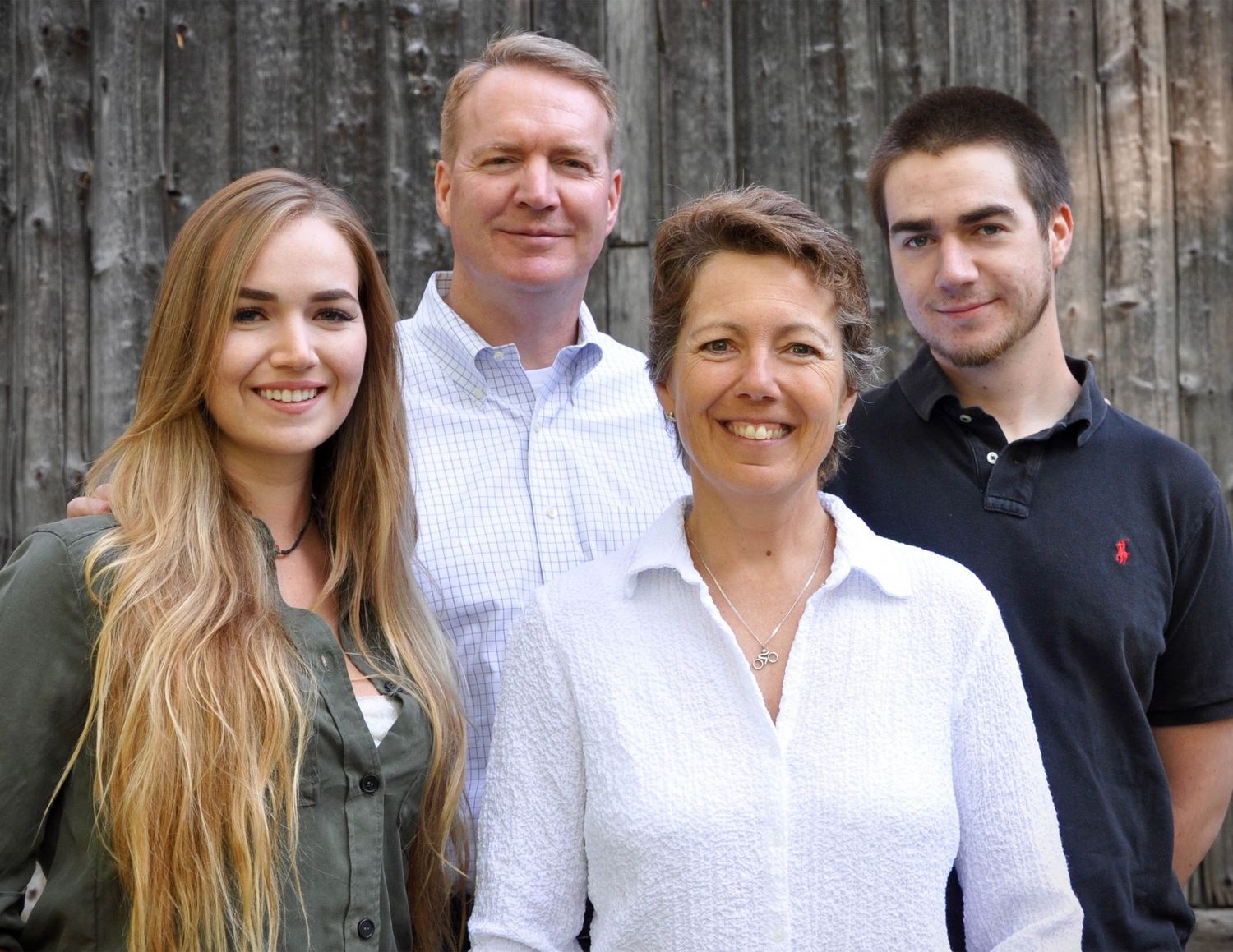 A family wearing casual attire pose together against a dark wooden wall background.