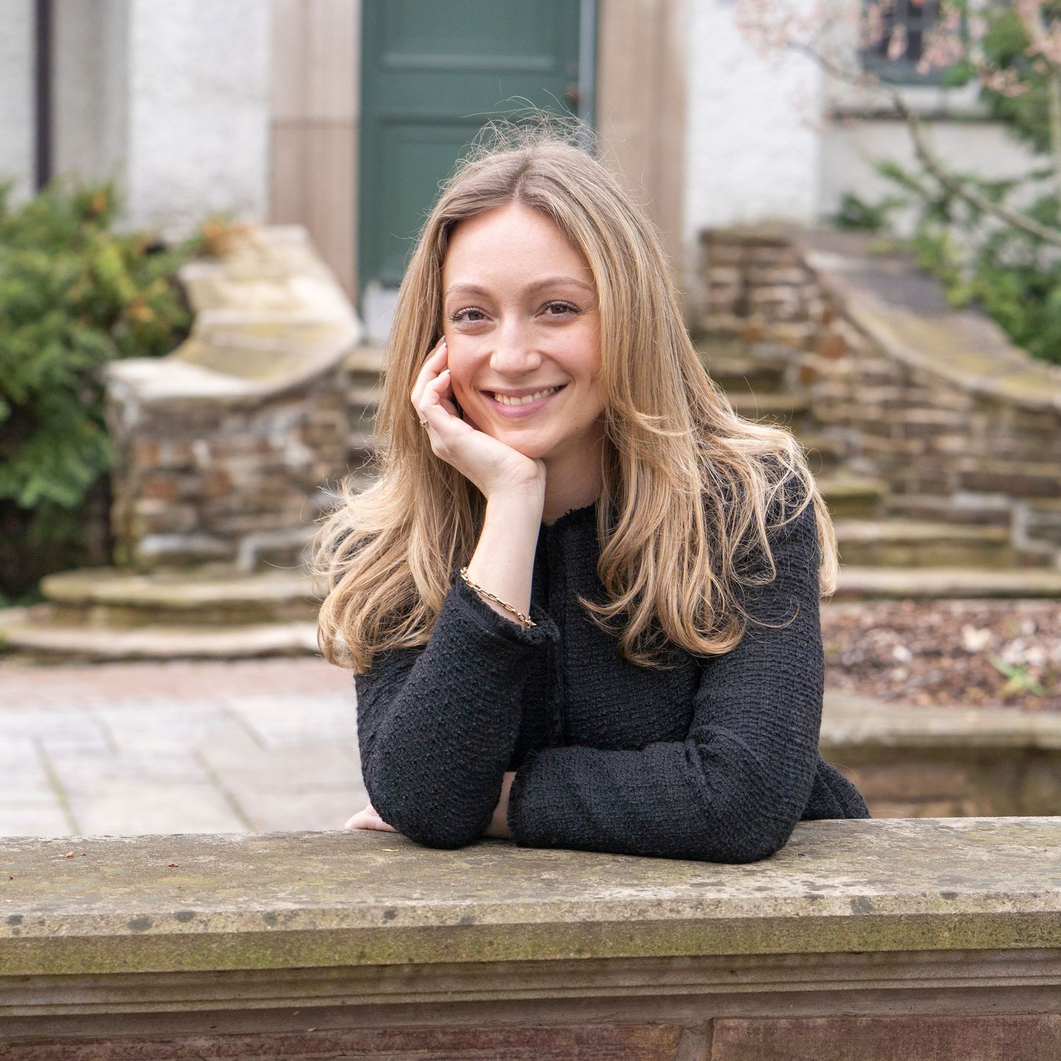 Professional outdoor portrait session featuring a casual pose on stone steps with a garden backdrop.