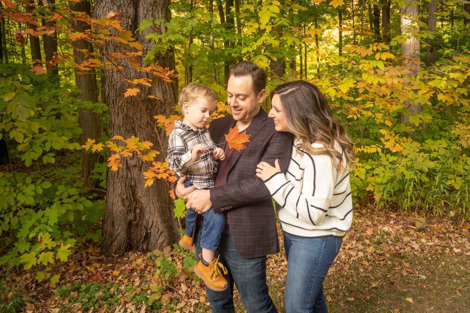 Family enjoying a warm autumn day together in a colorful forest setting during a photoshoot session.