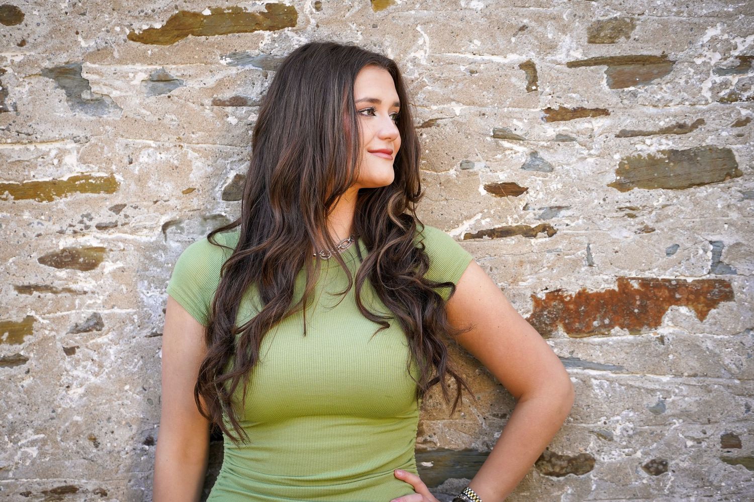 Person in a lime green top poses against a rustic stone wall in an outdoor portrait session.