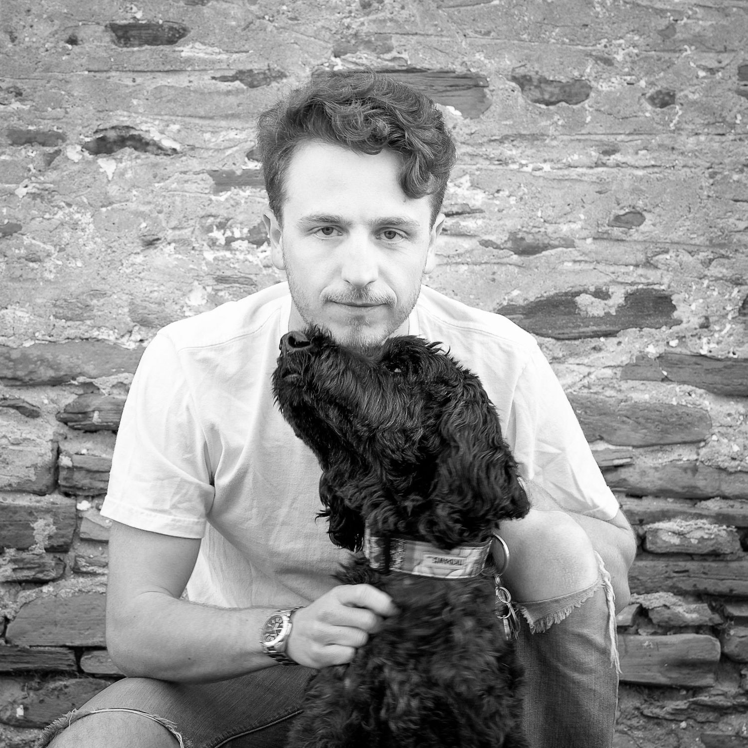 An emotional moment of connection between a young man and his black dog, as the dog leans his head into the young man.