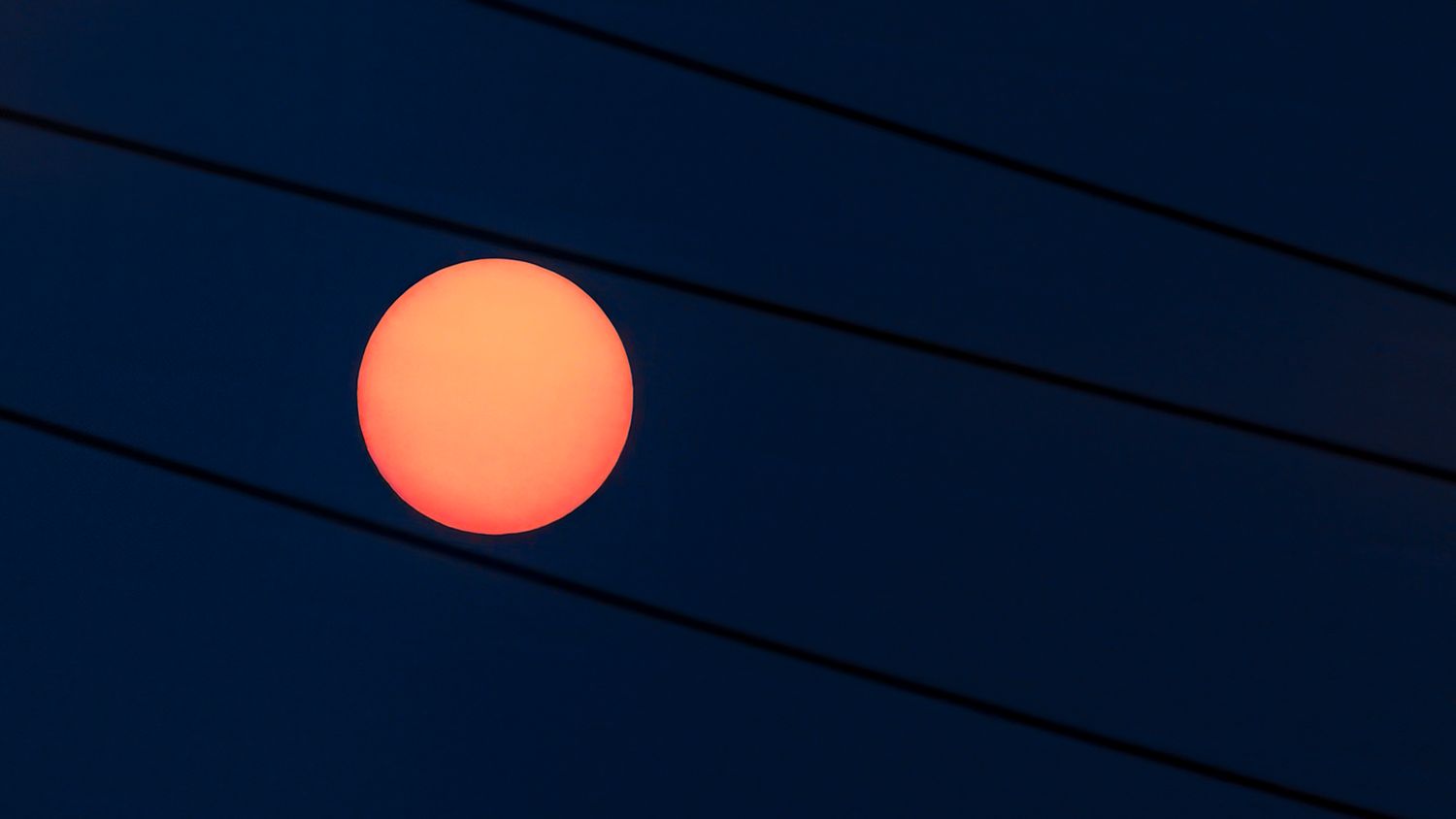 Glowing orange sun setting appears to dance along  power lines against a dark blue sky.