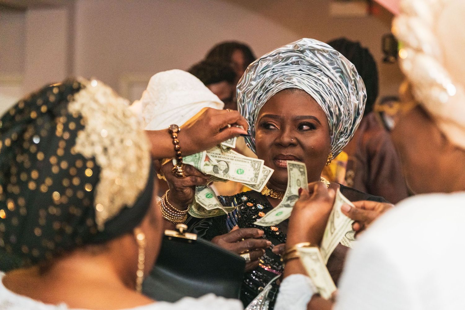 Guests in gold-embroidered gele spraying money at a West African celebration