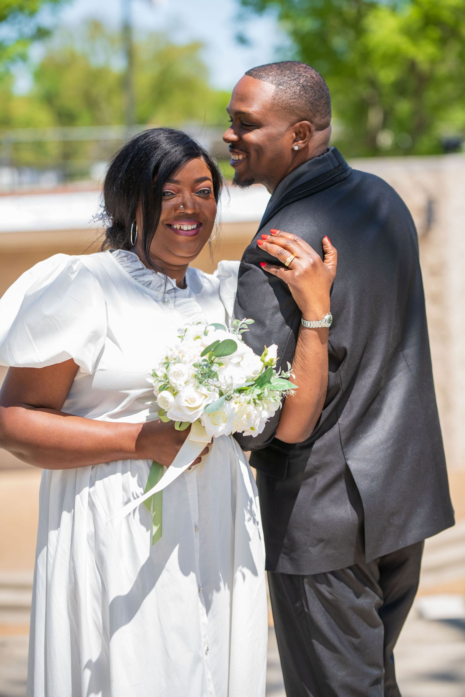 Bride in a white dress and groom in a black suit laughing outdoors on their wedding day