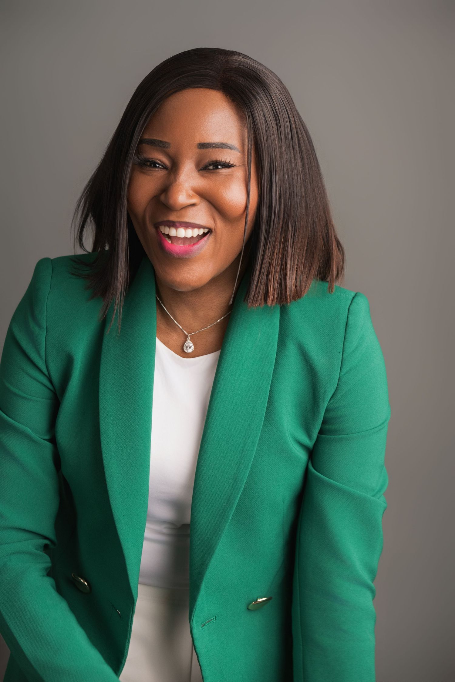Professional headshot of a woman in a green blazer against a gray studio backdrop