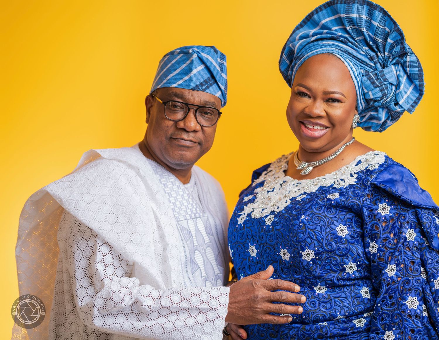Couple in Yoruba traditional dress and matching blue gele against a yellow studio backdrop