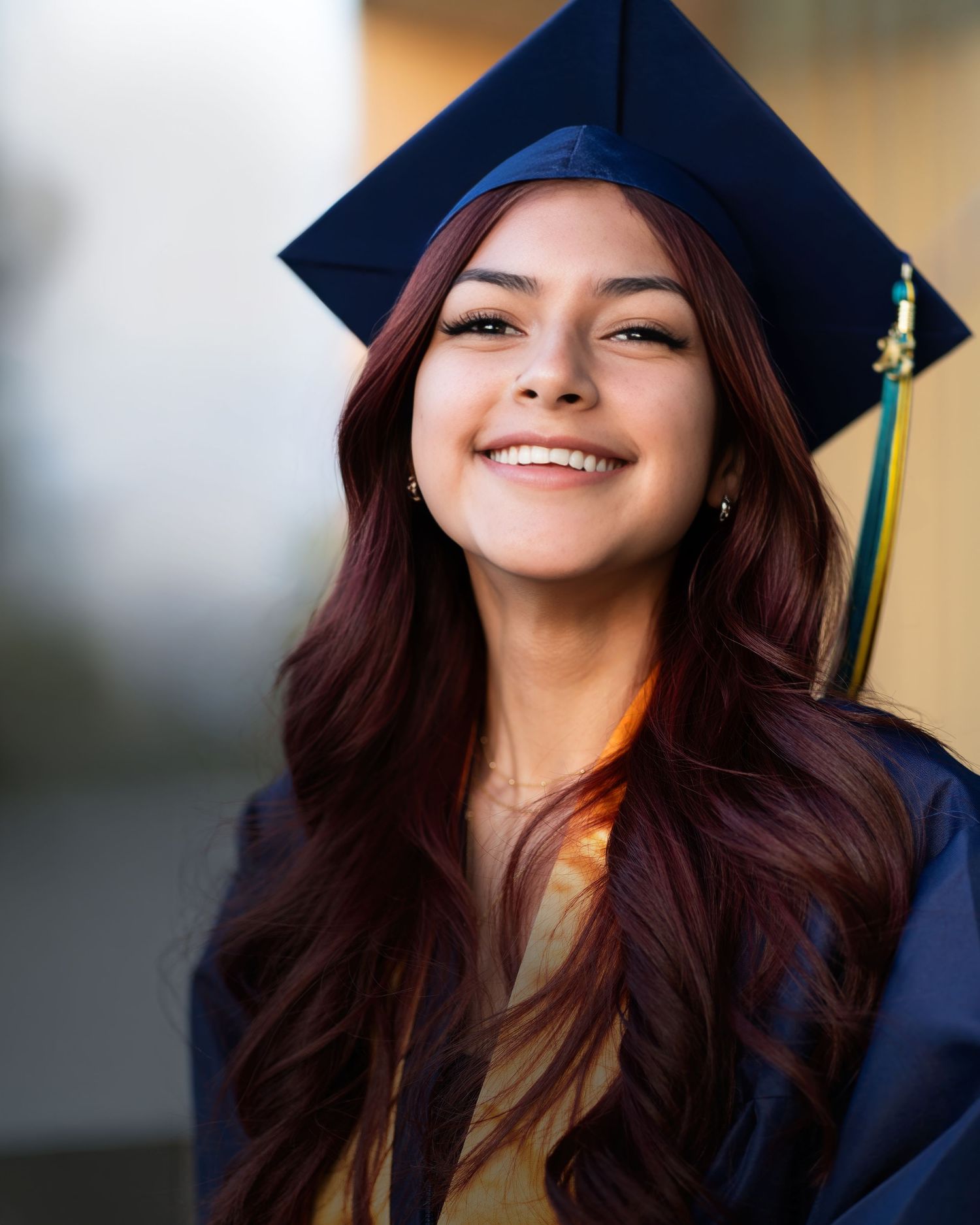 A young woman with long dark hair and a graduation cap smiles at the camera.