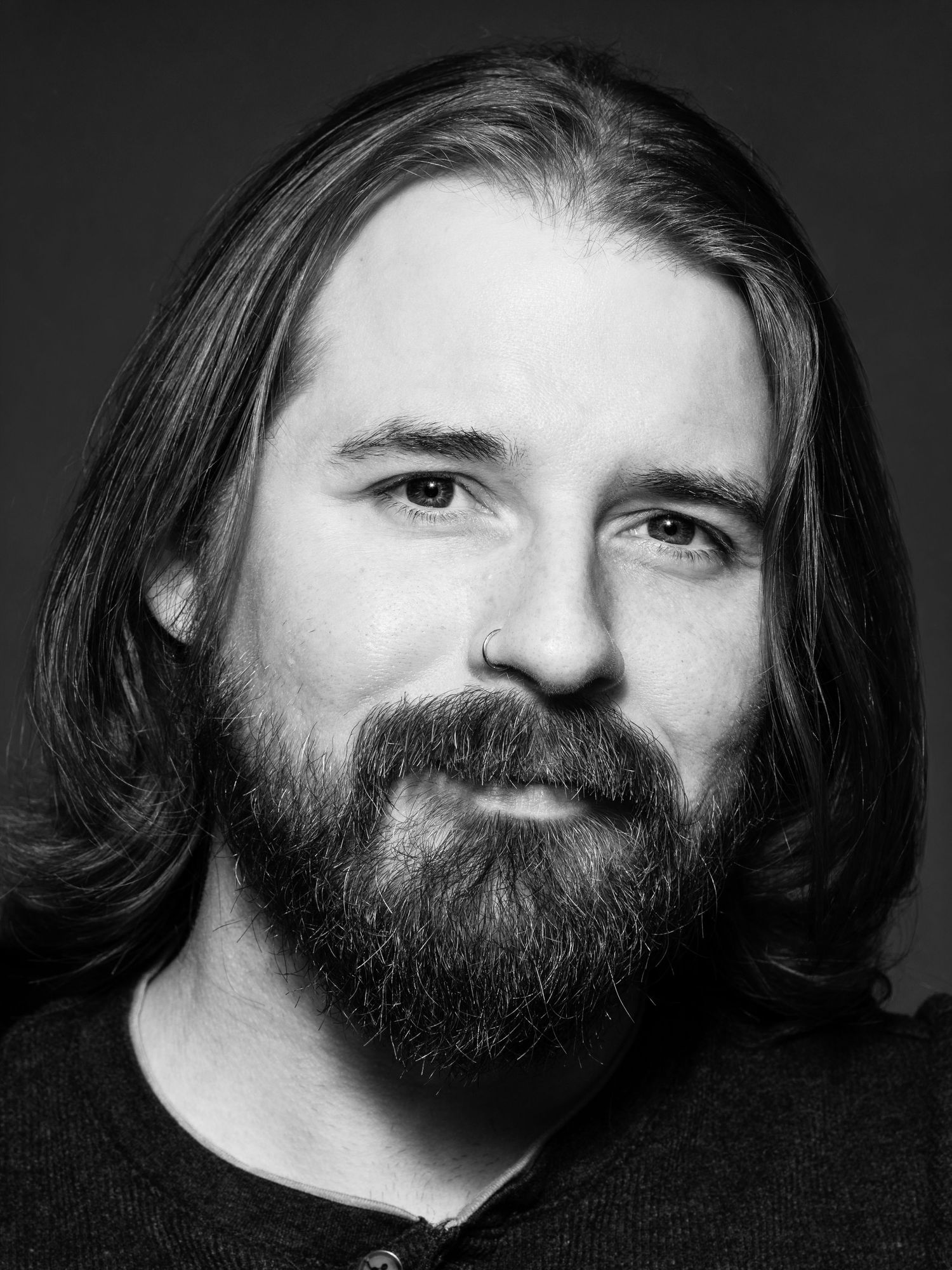 Black and white portrait of a bearded man with long hair, captured in a professional studio headshot.