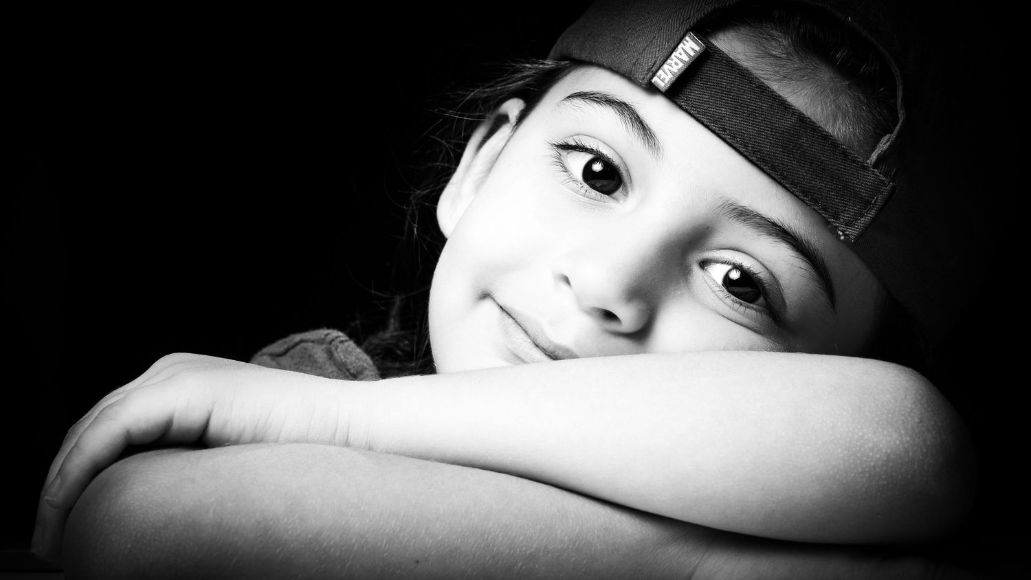 A close-up black and white portrait of a smiling child wearing a hat.