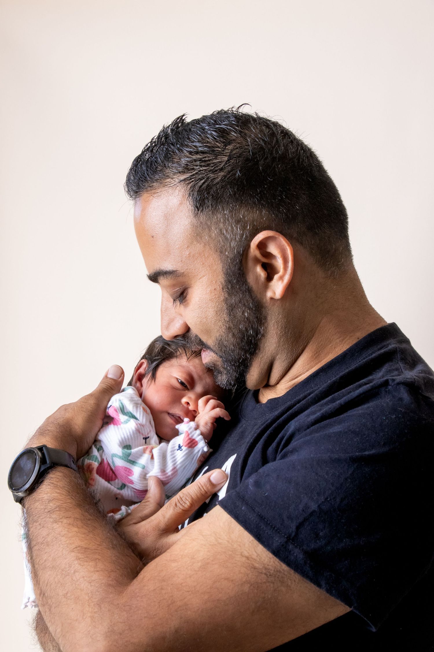 A bearded father tenderly holds and gazes at his newborn baby wrapped in a floral swaddle blanket.