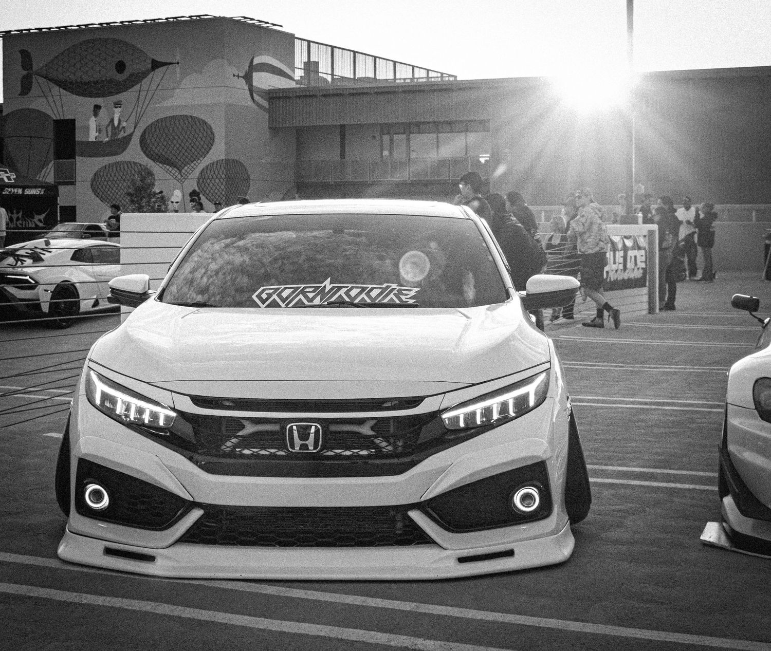 Black and white photo of a modified Honda Civic at a car show, featuring custom body kit and LED headlights.