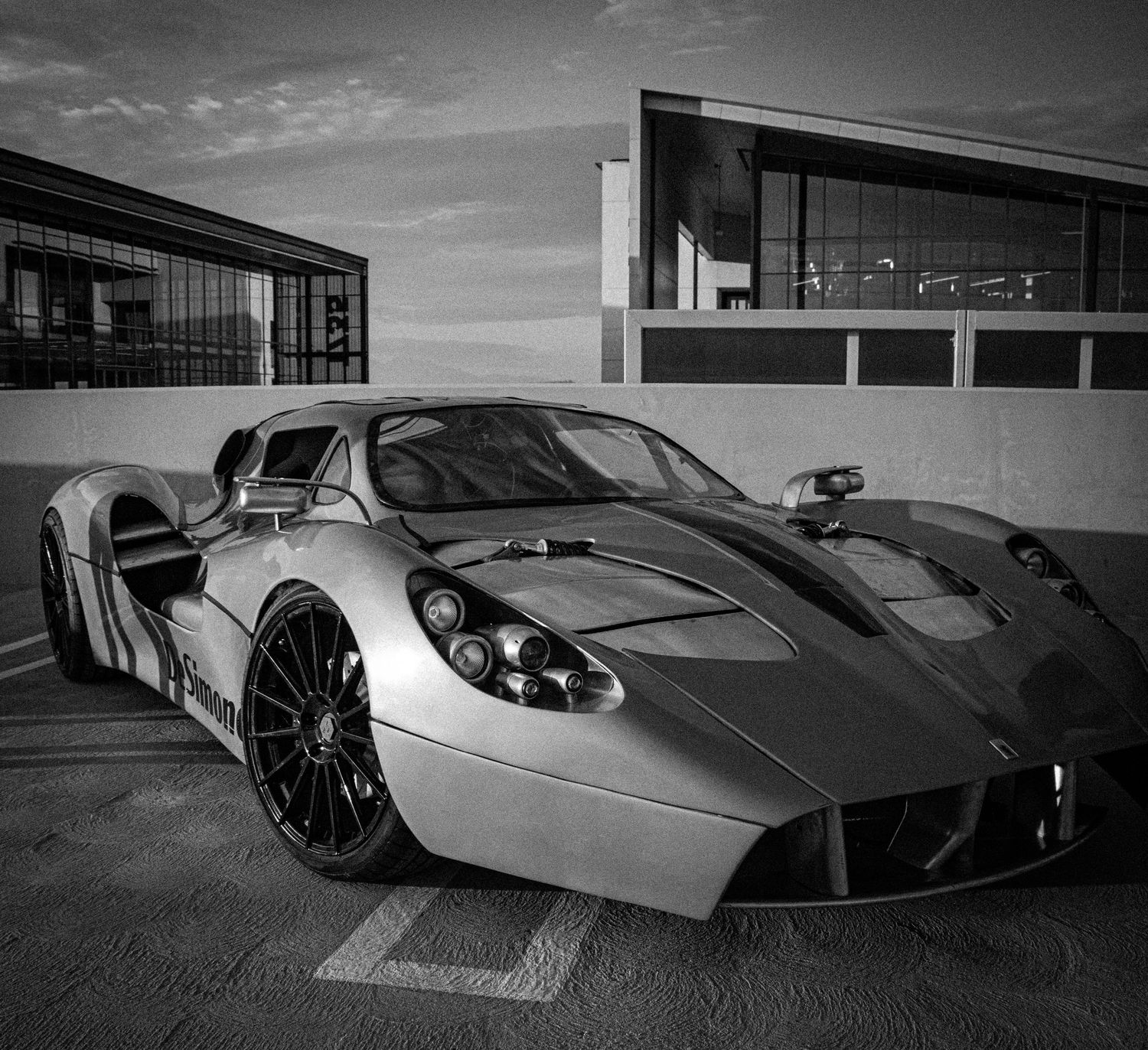Sleek silver supercar parked outside modern building in dramatic black and white photography.