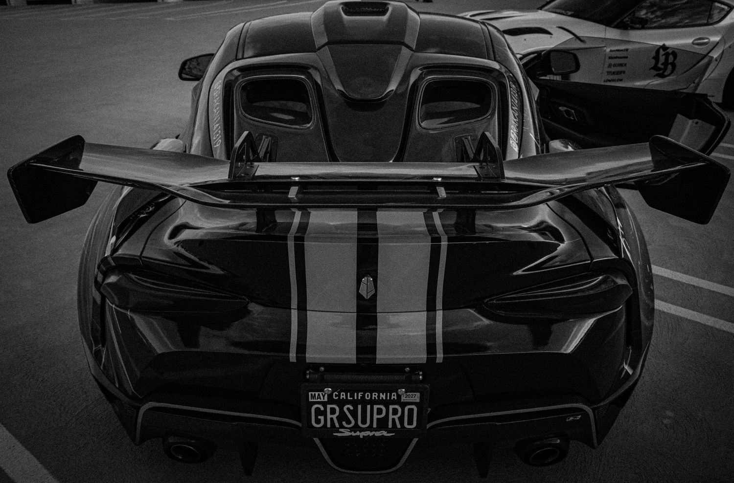 Black and white rear view of a sleek sports car with GRSUPRO California license plate and racing stripes.