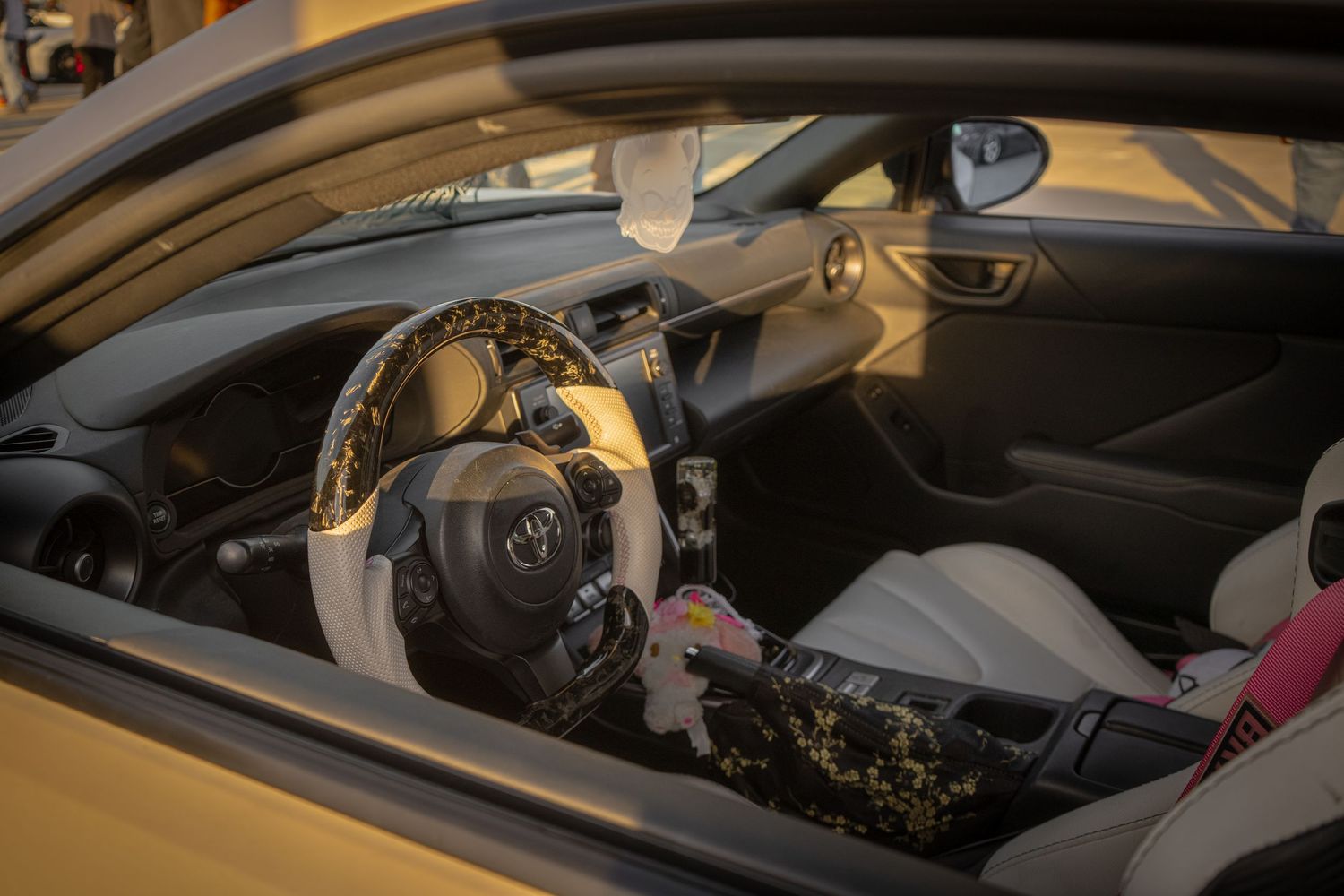 Interior view of a Toyota car with decorative floral steering wheel cover and custom seat covers visible through window.