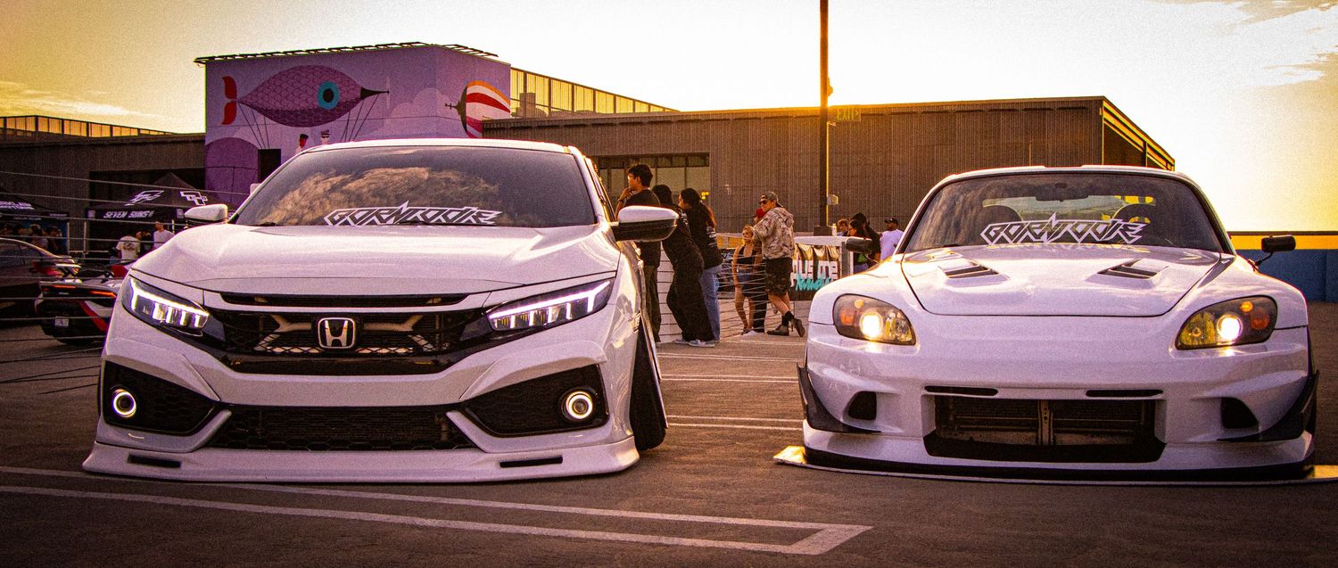 Two white modified Honda cars with wide body kits parked side by side at a car show during golden hour.