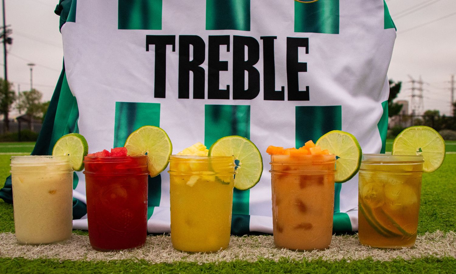 Vibrant cocktails with citrus garnishes lined up against a striped backdrop outdoors.