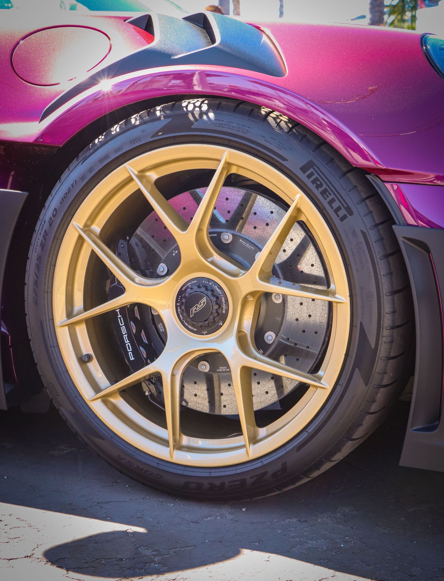 Close-up of gold sports car wheel with pink body and performance brake system.