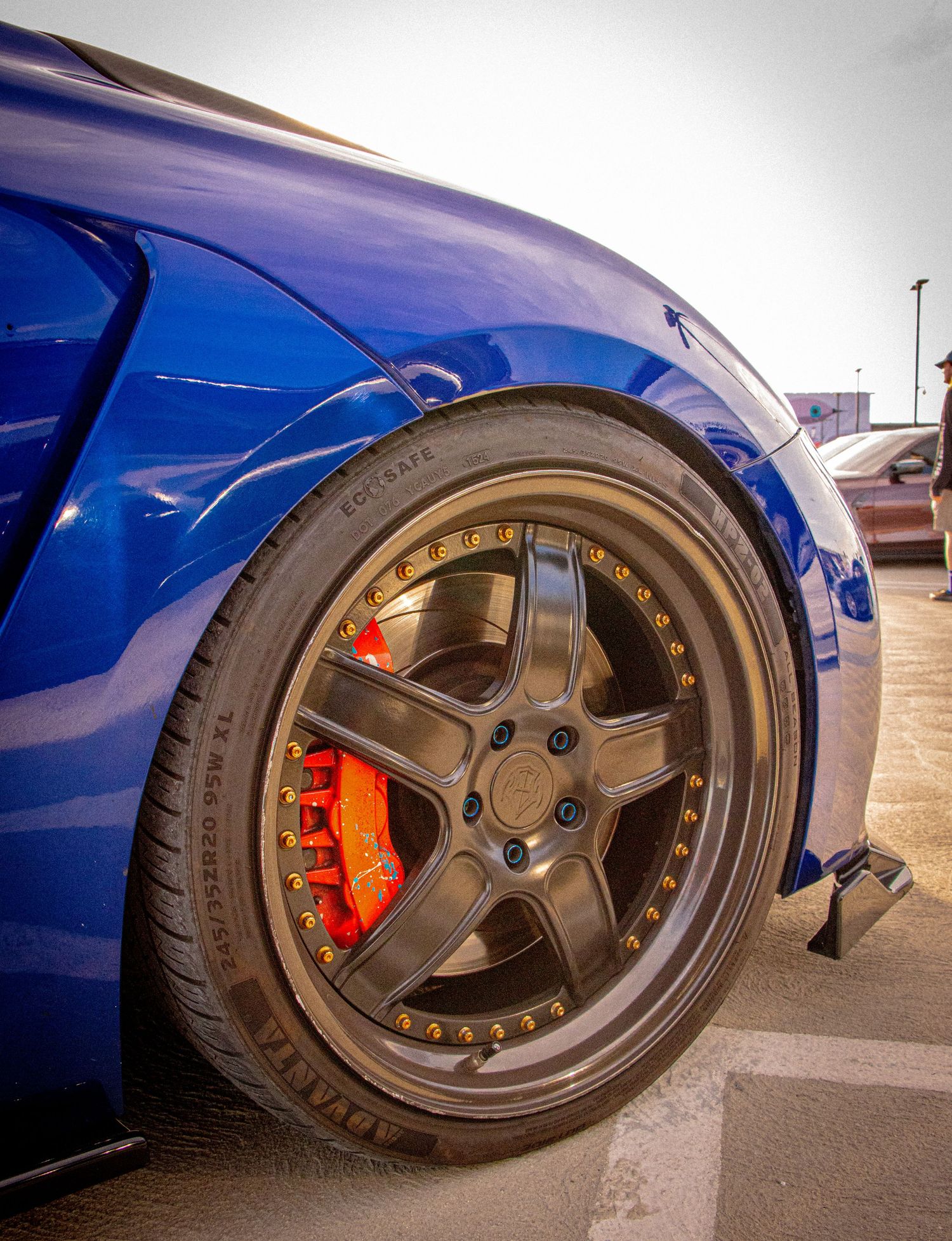 Close-up of a blue sports car featuring bronze multi-spoke wheels with gold bolts and bright red brake calipers.