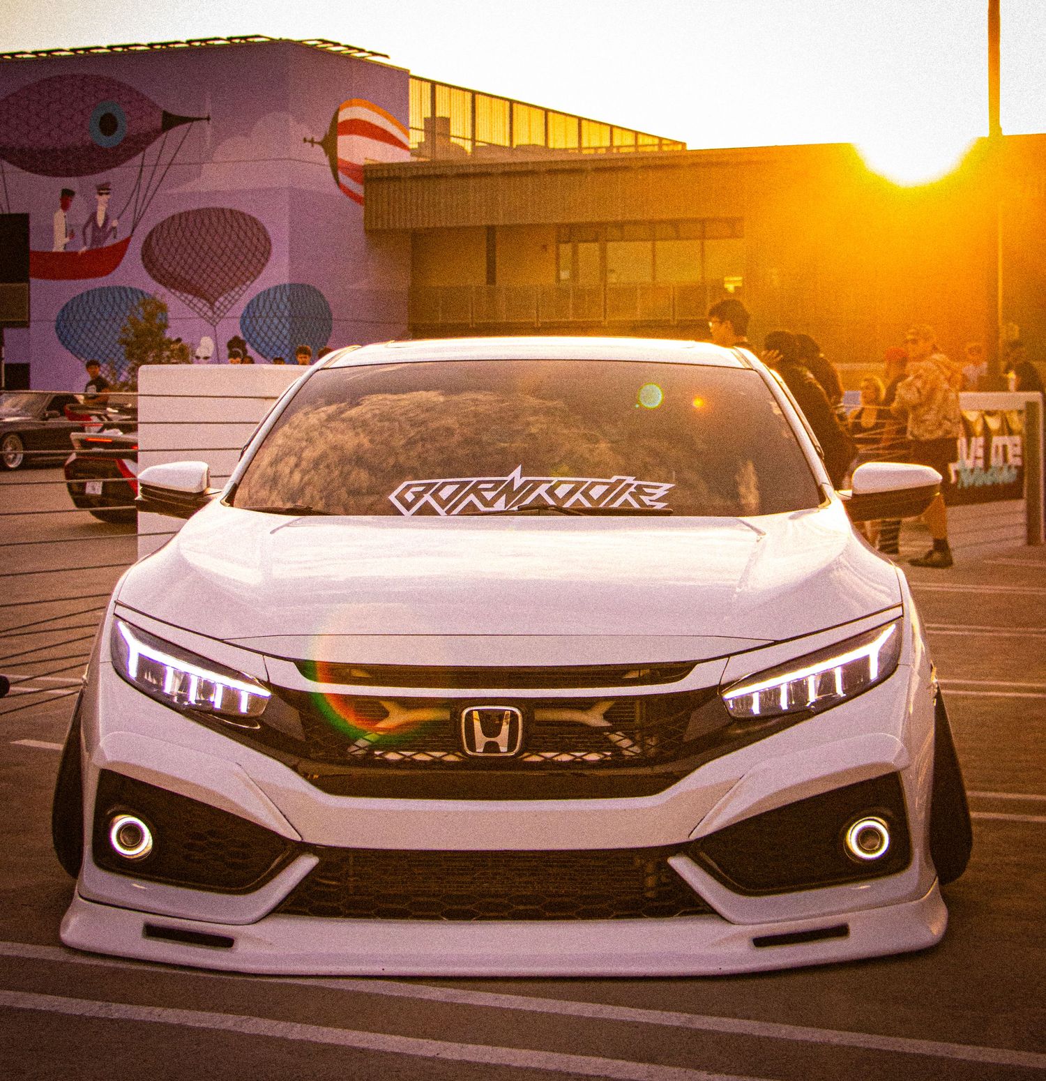 White Honda Civic with custom body kit and LED headlights at golden hour in a parking lot.