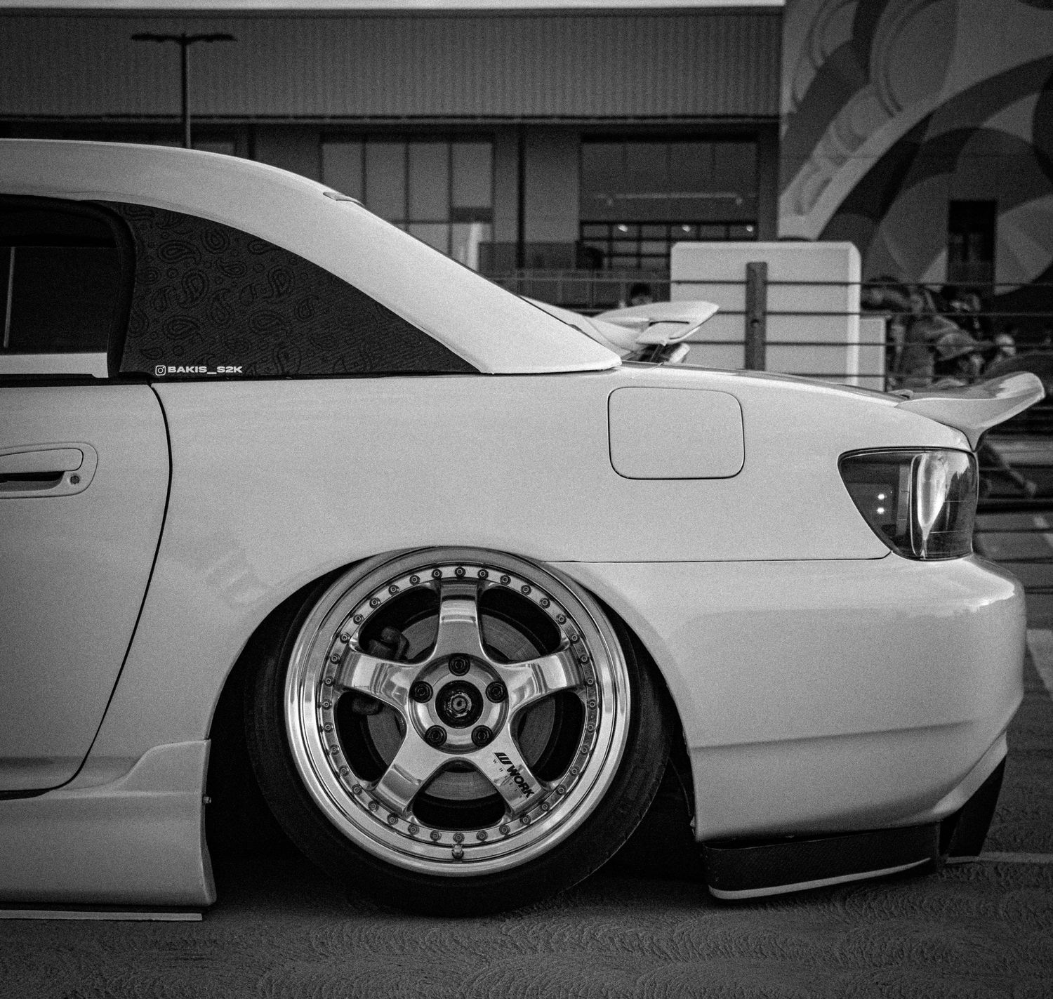 Black and white photo of a lowered white car with deep-dish aftermarket wheels on a parking lot.