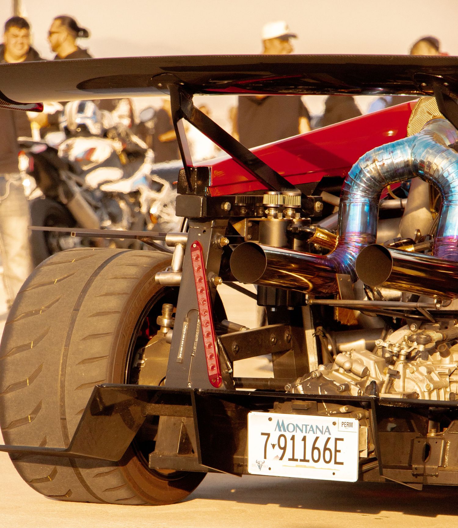Custom Montana-plated dragster with exposed engine, turbo pipes, and wide rear tire at a racing event.