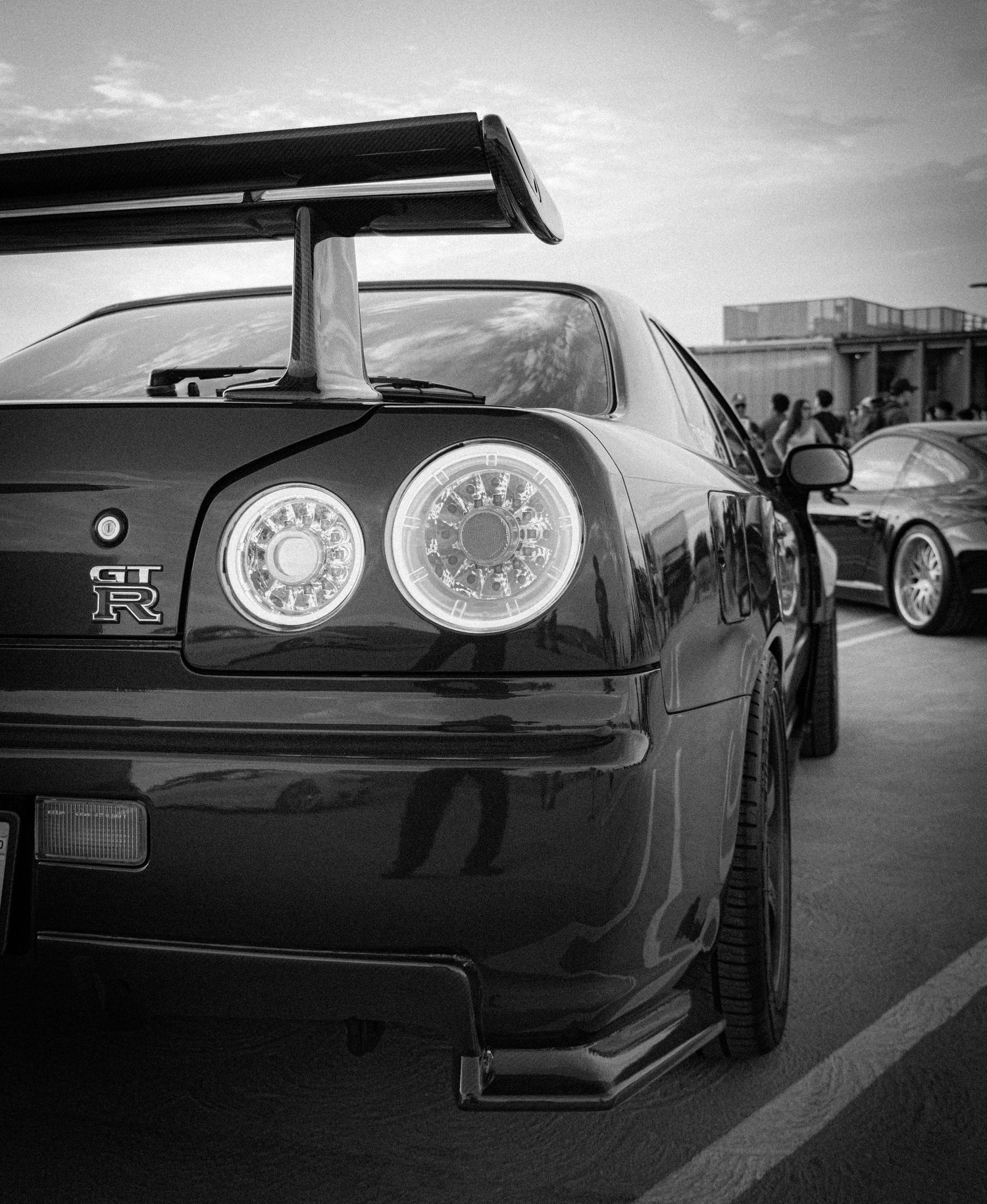 Black and white photo of a Nissan Skyline GT-R rear view showcasing taillights and spoiler at a car show.