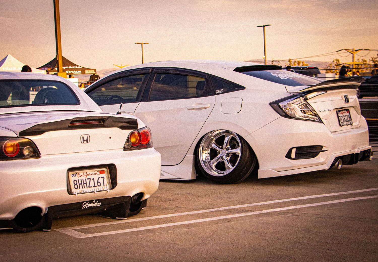 Two modified white Honda cars parked in a lot, featuring lowered suspension and custom wheels at a car meet.