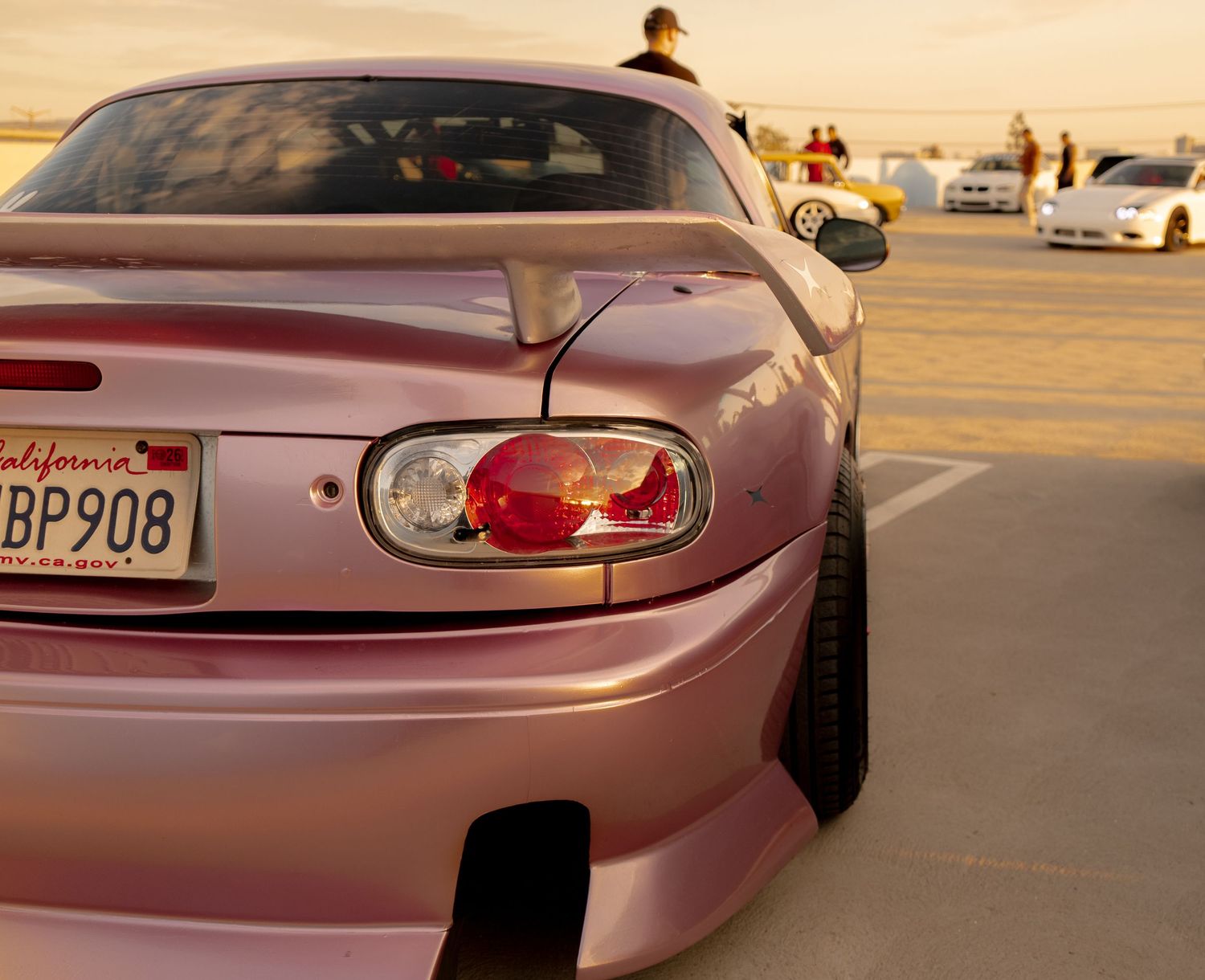 Pink Toyota Supra with California license plate BP908 at a car meet, showcasing custom wide body kit and taillights.